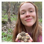 A young, red haired woman, smiles and holds out a handful of morel mushrooms